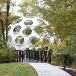 domed art structure that looks like soccer ball off crystal bridge path among trees