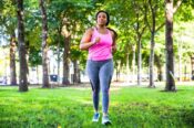 woman in exercise clothes walking through park listening to music through ear buds
