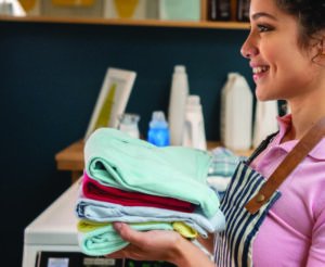 profile of woman smiling as she holds a stack of folded laundry