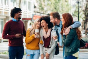diverse group of millennials on a city street drinking coffee and laughing