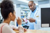 male pharmacist pointing to prescription label and talking to female patient