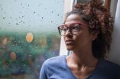 somber young woman looking out window on rainy day