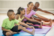 A family is sitting on exercise mats and stretching out their legs during a yoga class