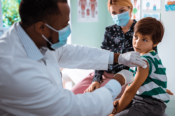 doctor with mask giving flu shot to child
