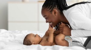 Woman and a baby laying on a bed as she smiles looking down at the baby