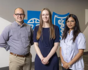 Arkansas Blue Cross and Blue Shield summer interns Dillon Cordel, Lauren LeRoy, and Sayli Naik stand in front of the cross and shield.